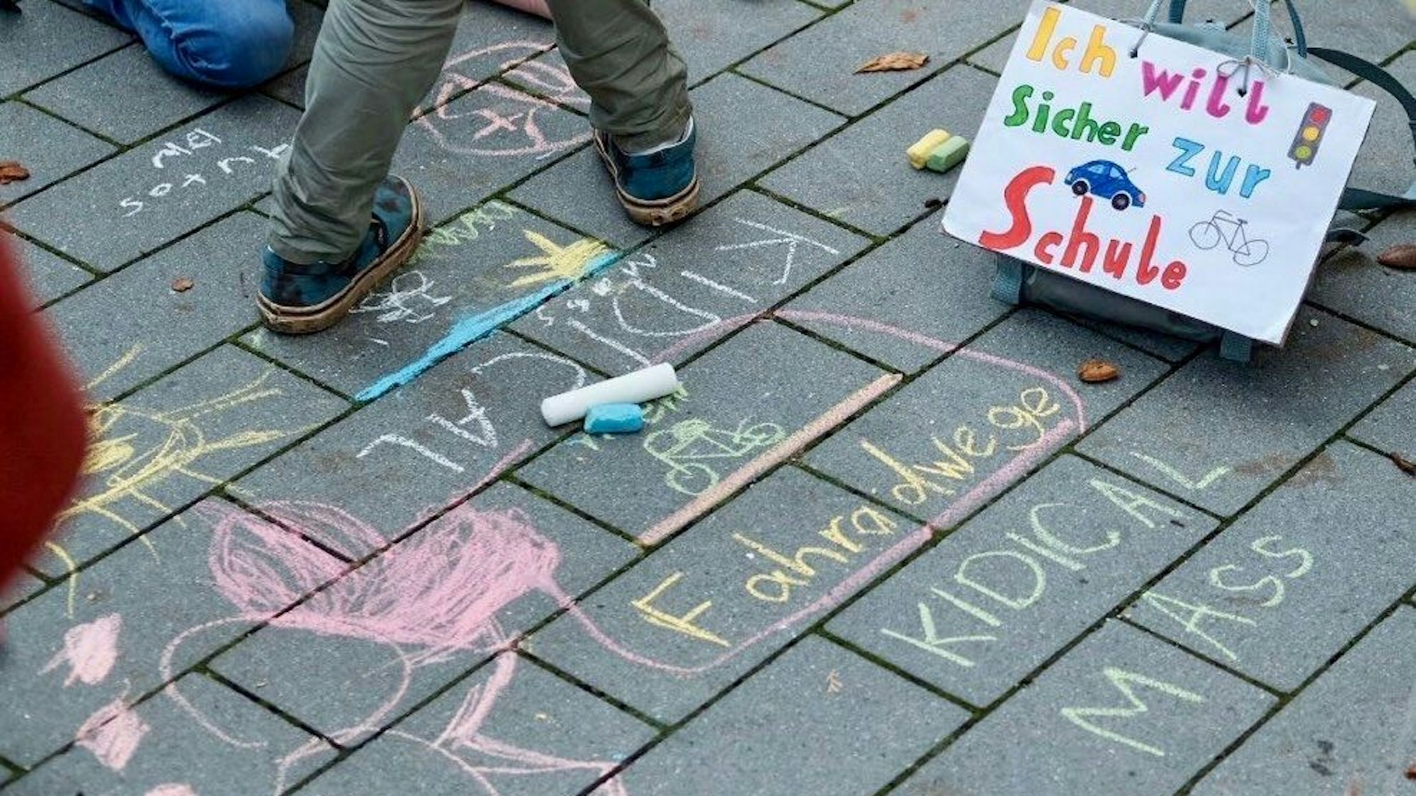 Auf der Straße steht ein von Kindern gemaltes Plakat, auf dem steht: „Ich will sicher zur Schule“.