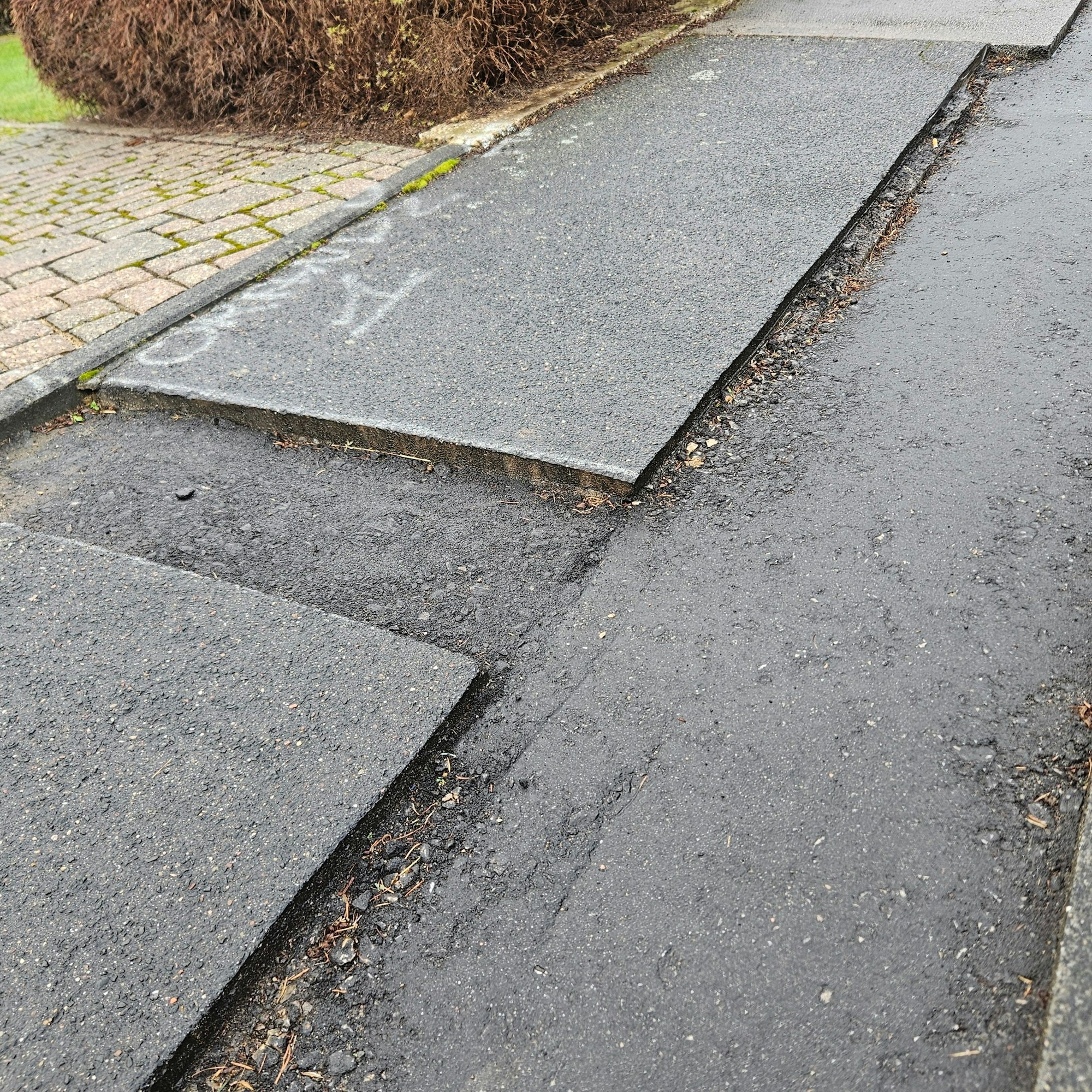 Zu sehen ist ein Bürgersteig mit scharfen Kanten an den Stellen, an denen Asphalt fehlt.