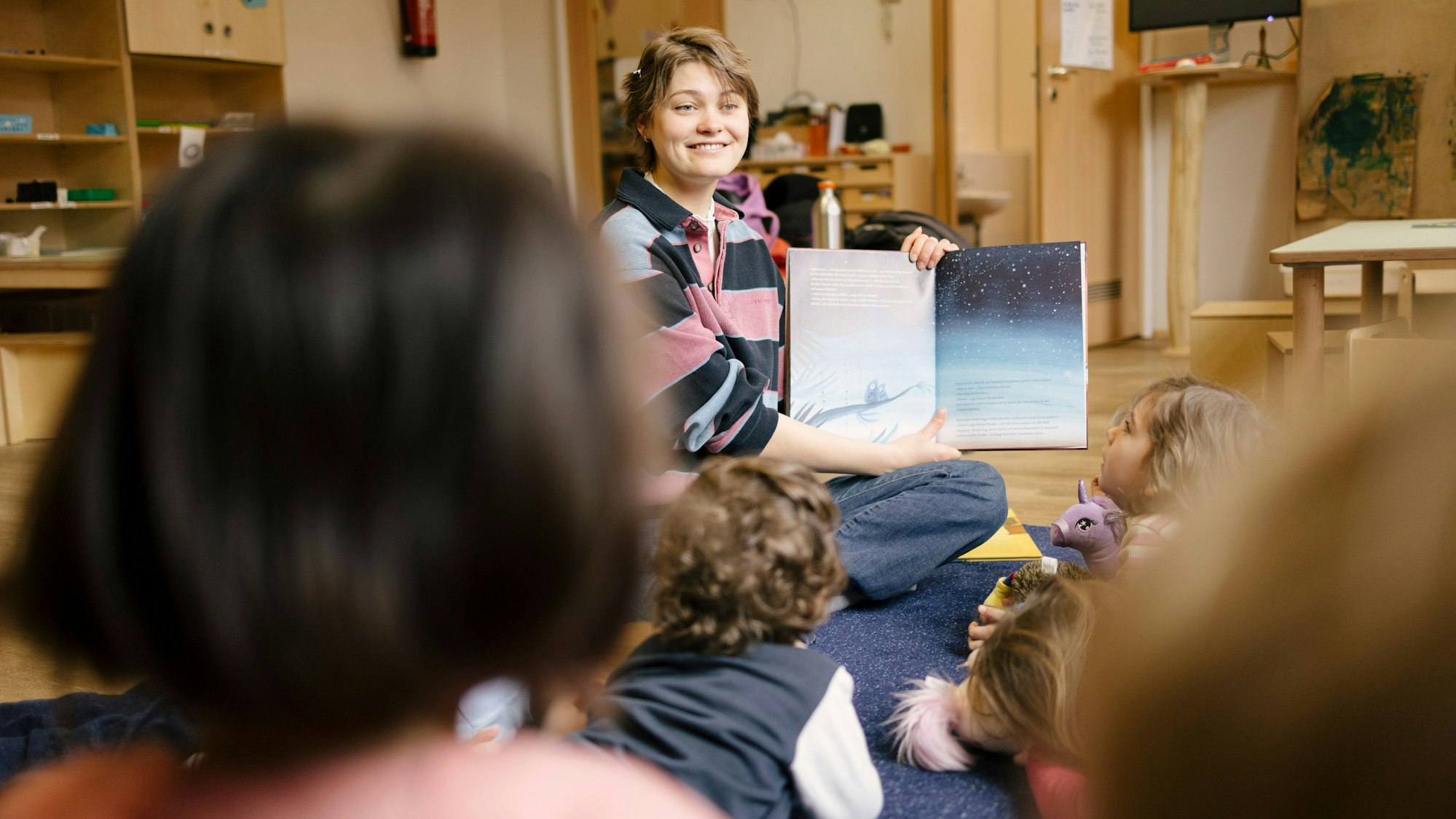 Eine junge Frau liest Kita-Kindern vor.