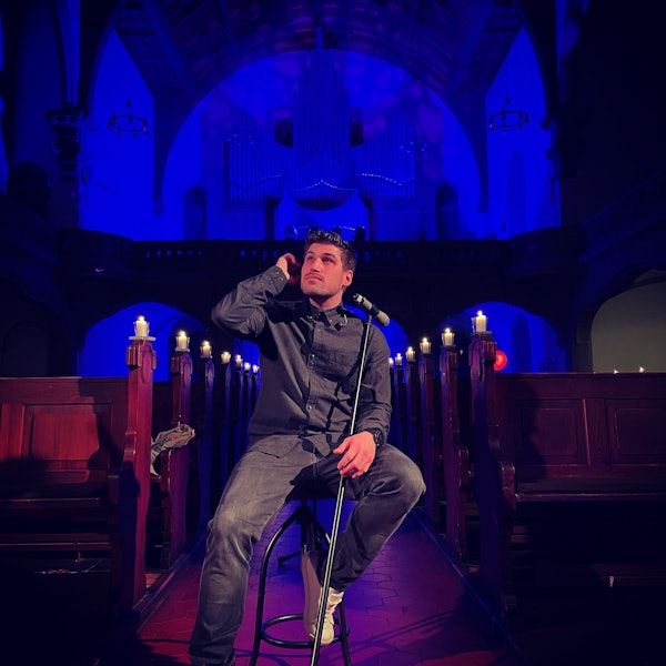 Dominic Sanz posiert in der Mannheimer Friedenskirche auf einem Stuhl hinter einem Mikrofon und schaut in die Ferne.