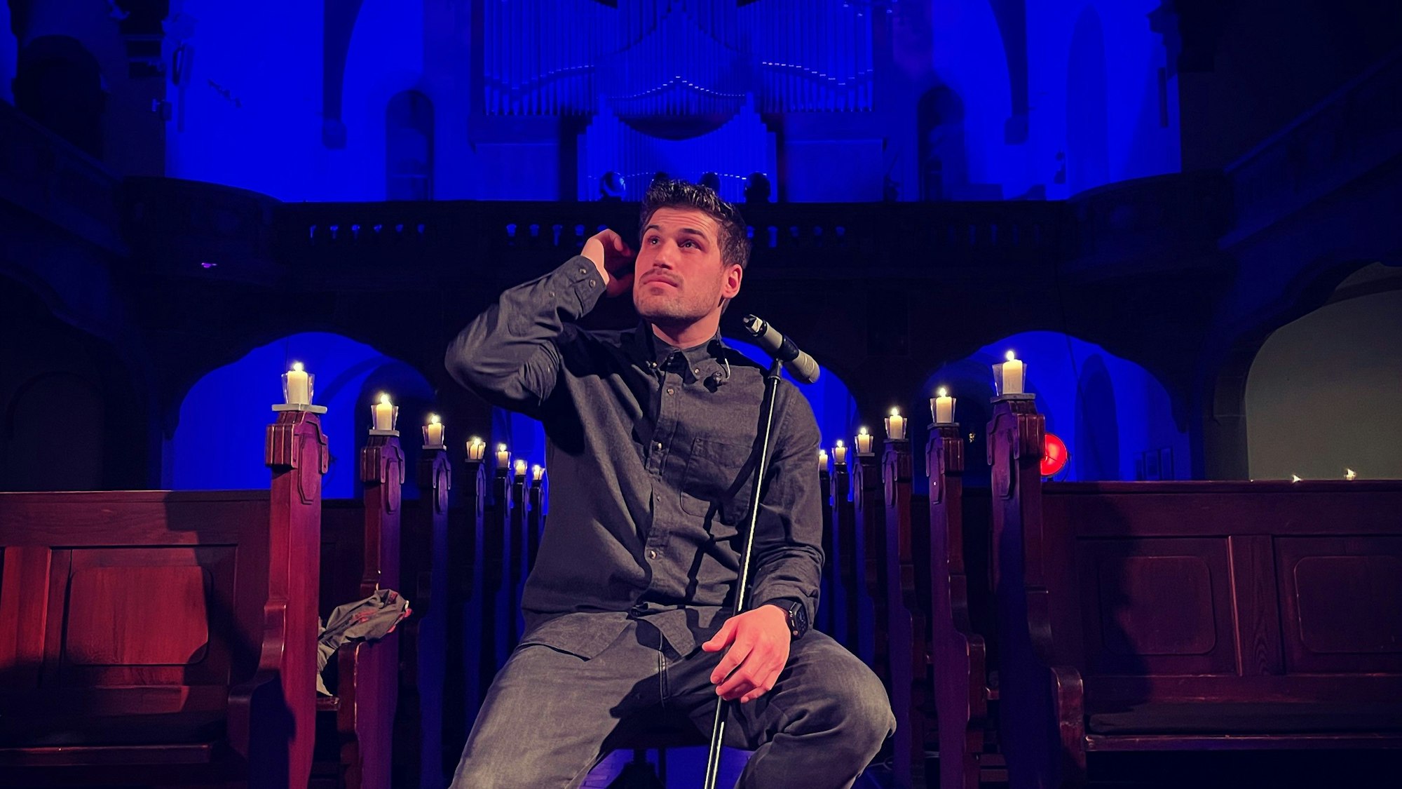 Dominic Sanz posiert in der Mannheimer Friedenskirche auf einem Stuhl hinter einem Mikrofon und schaut in die Ferne.