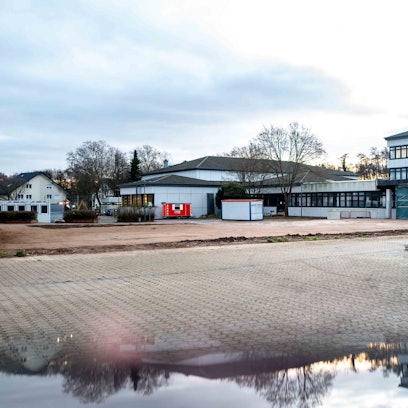 Blick auf das Thomas-Eßer-Berufkolleg in Euskirchen. Das Gebäude spiegelt sich in einer Pfütze auf dem Schulhof.
