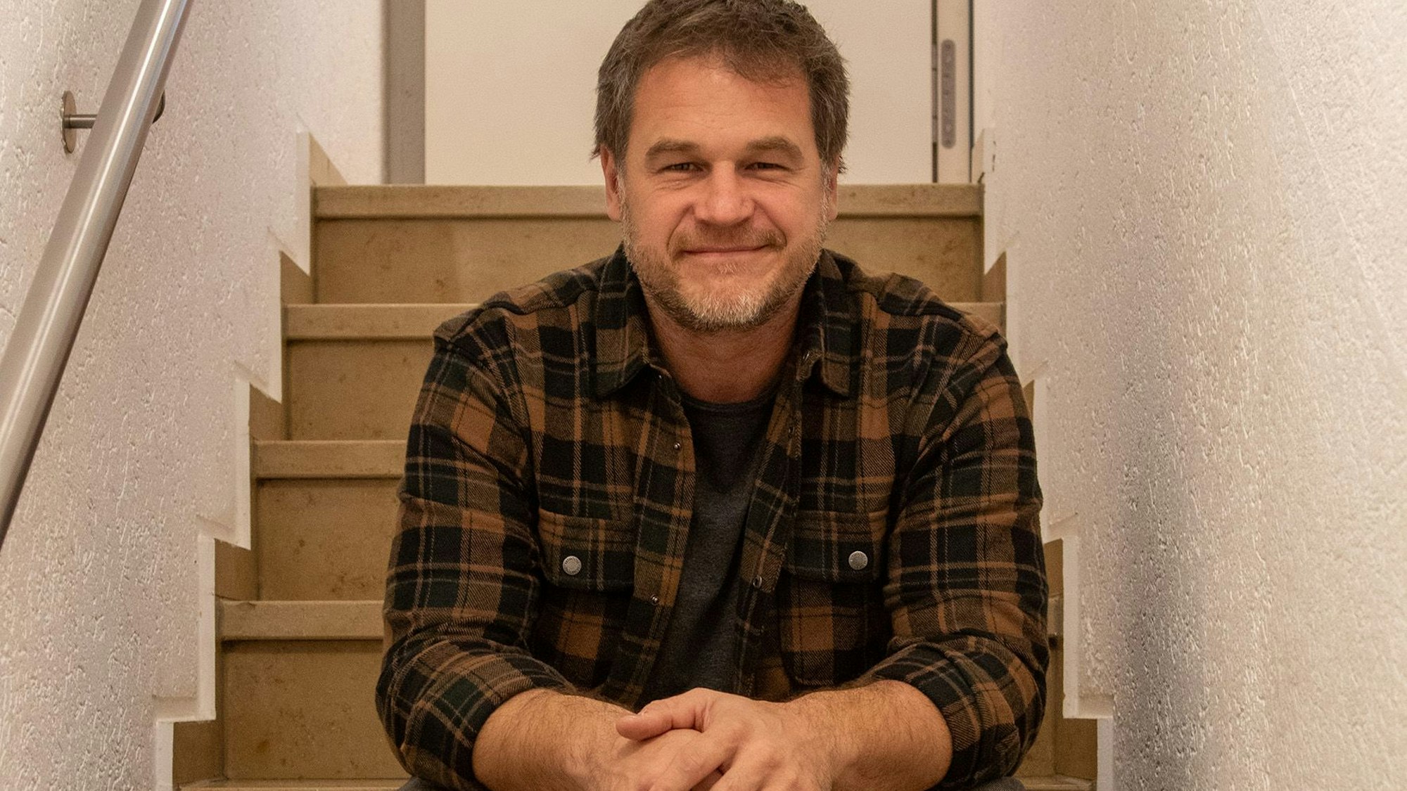 Christian Golz sitzt auf einer Treppenstufe und lächelt in die Kamera.