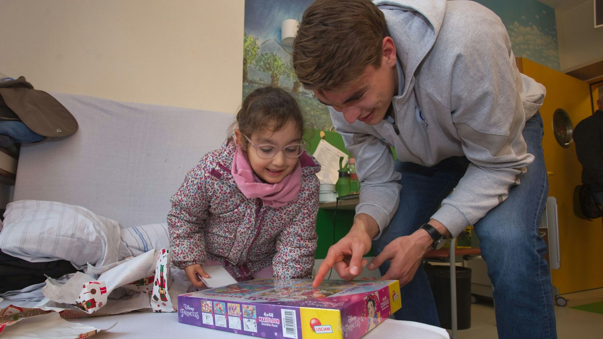 Ein Handballer packt mit einem kleinen Mädchen ein Geschenk aus.