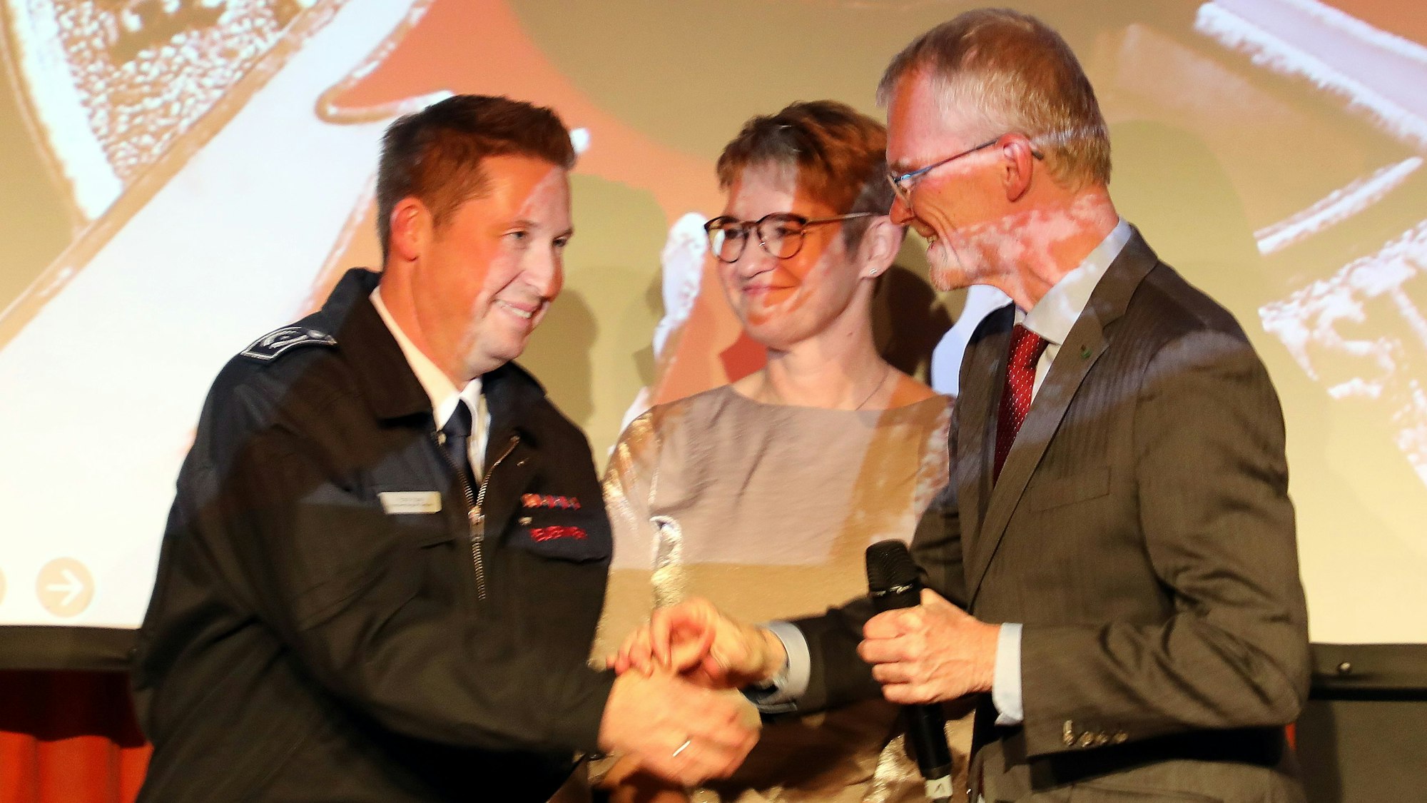 Frank und Nicole Haag stehen mit Bürgermeister Frank Stein auf der Bühne des Spiegelsaals im Bergischen Löwen.