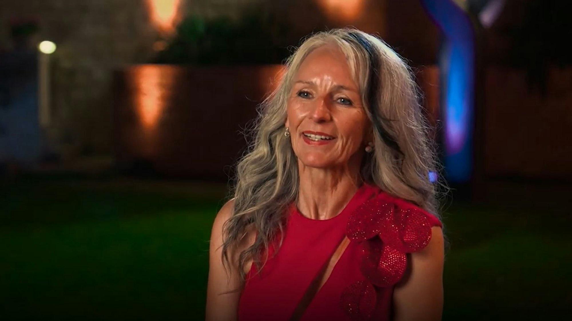 Sabine aus Troisdorf ist Kandidatin bei der RTL-Dating-Show Golden Bachelor. Hier schaut sie links an der Kamera vorbei, trägt ein rotes Kleid.