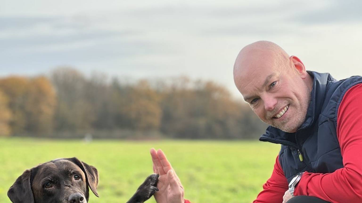 Manni Hartmann und sein Hund grüßen sich mit Hand und Pfote.
