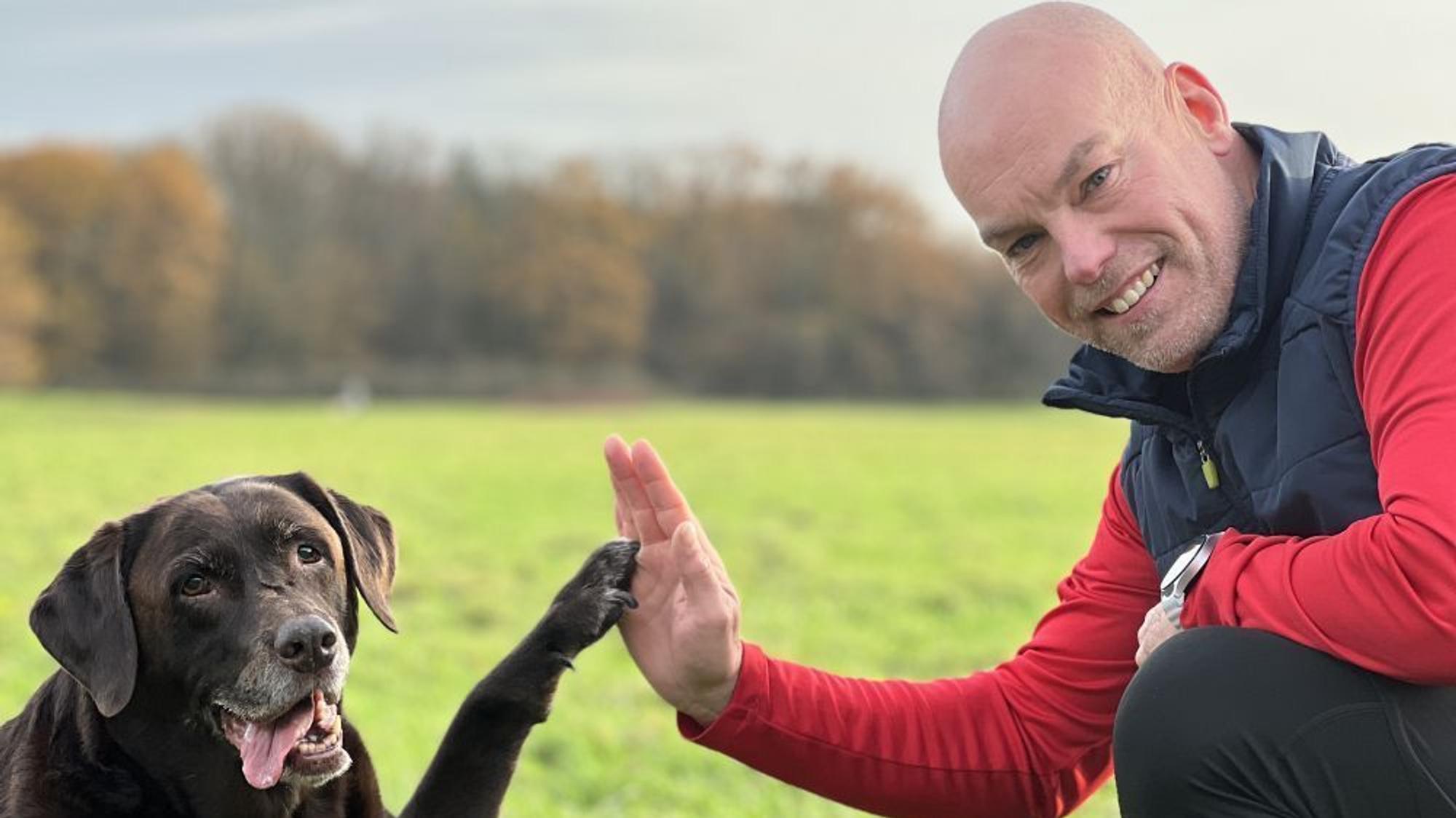 Manni Hartmann und sein Hund grüßen sich mit Hand und Pfote.