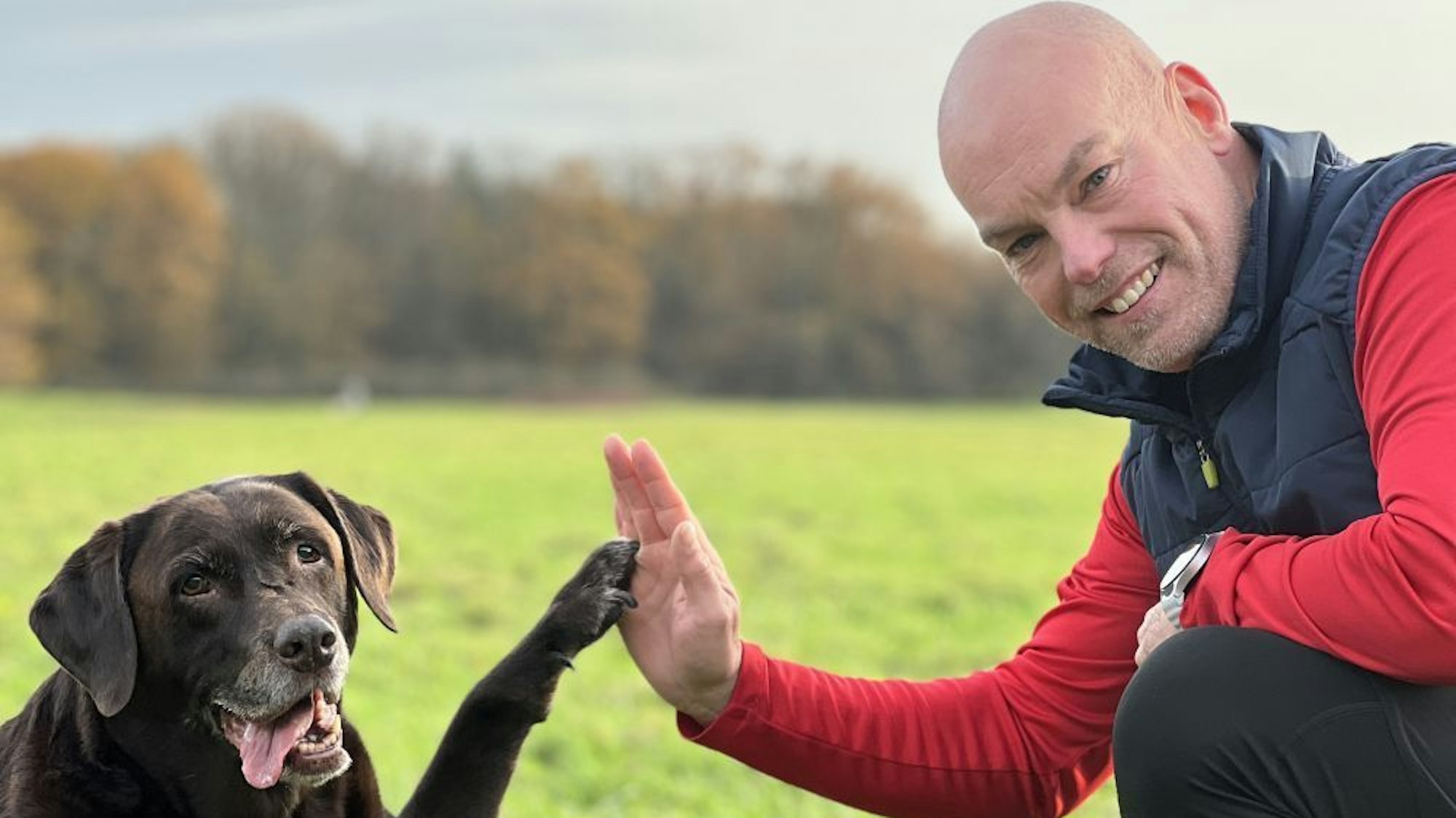 Manni Hartmann und sein Hund grüßen sich mit Hand und Pfote.