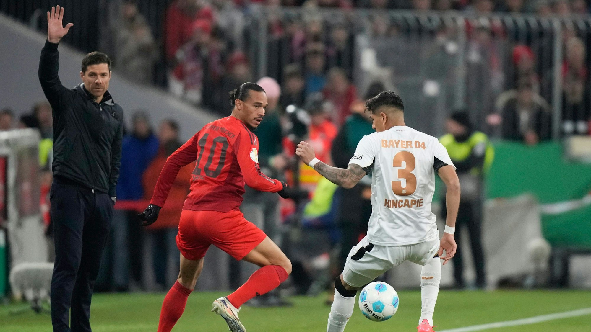Leverkusens Trainer Xabi Alonso (l.), Bayer-Verteidiger Piero Hincapie (r.) und Münchens Leroy Sane.