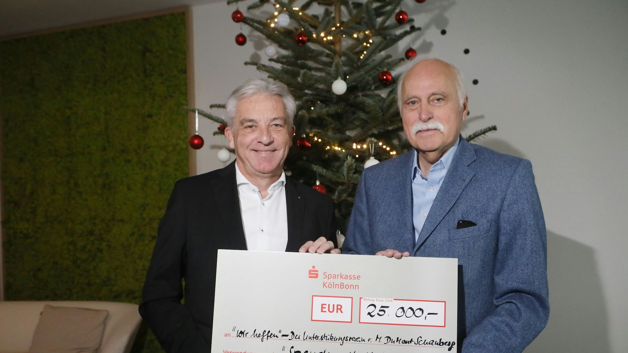 Das Vorstandsmitglied der Sparkasse Köln-Bonn, Rainer Virnich, überreicht einen großen symbolischen Papp-Scheck über 25.000 Euro Check an den „wir helfen“-Geschäftsführer Karl-Heinz Goßmann.