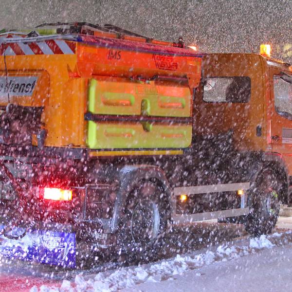 Ein Schneepflug räumt eine glatte schneebedeckte Straße.