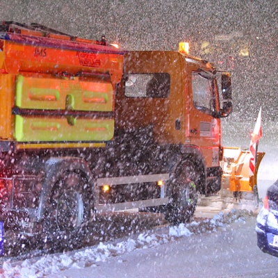 Ein Schneepflug räumt eine glatte schneebedeckte Straße.