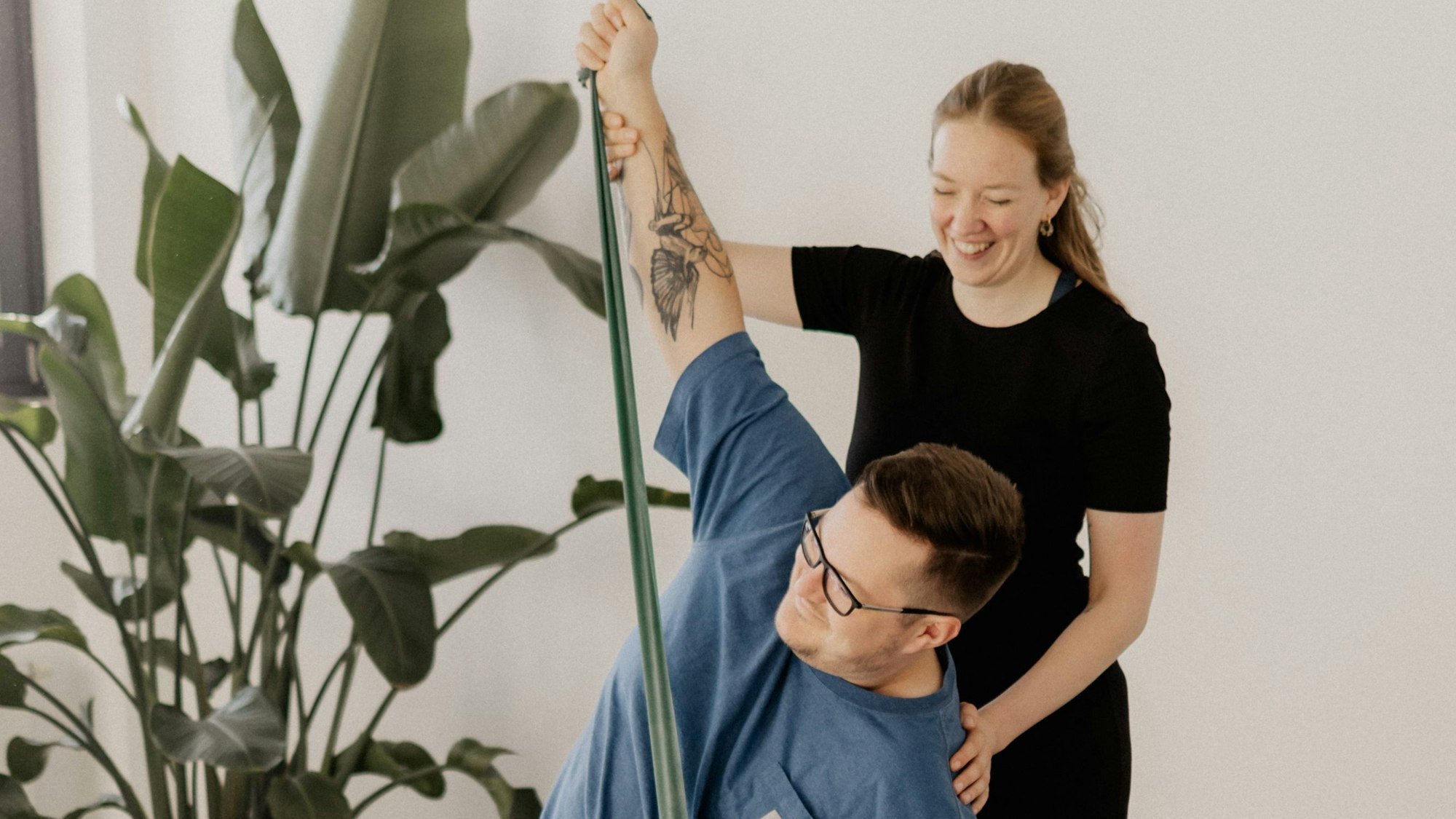 Das Bild zeigt eine Yoga-Lehrerin, die mit einem Mann eine Übung im Sitzen durchführt.