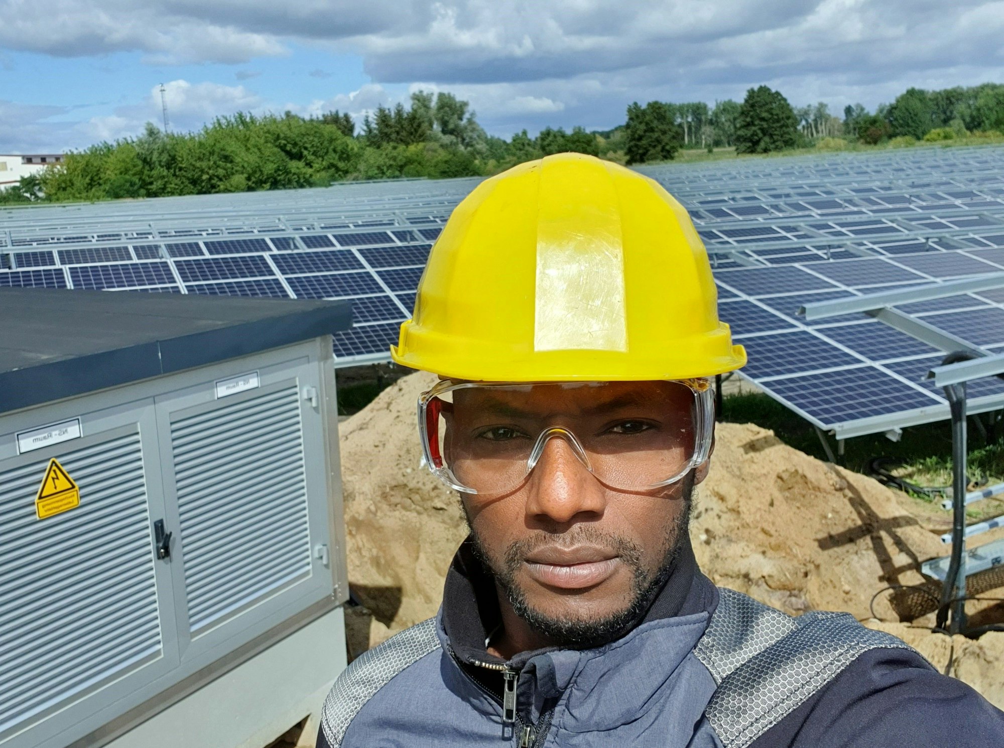 Porträt von Alhassane Barry vor einem Solarpark. Er trägt Helm und Schutzbrille.