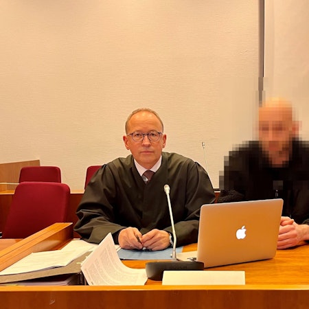 Zwei Männer sitzen an einem Tisch, auf dem ein Mikrofon und ein Laptop stehen.