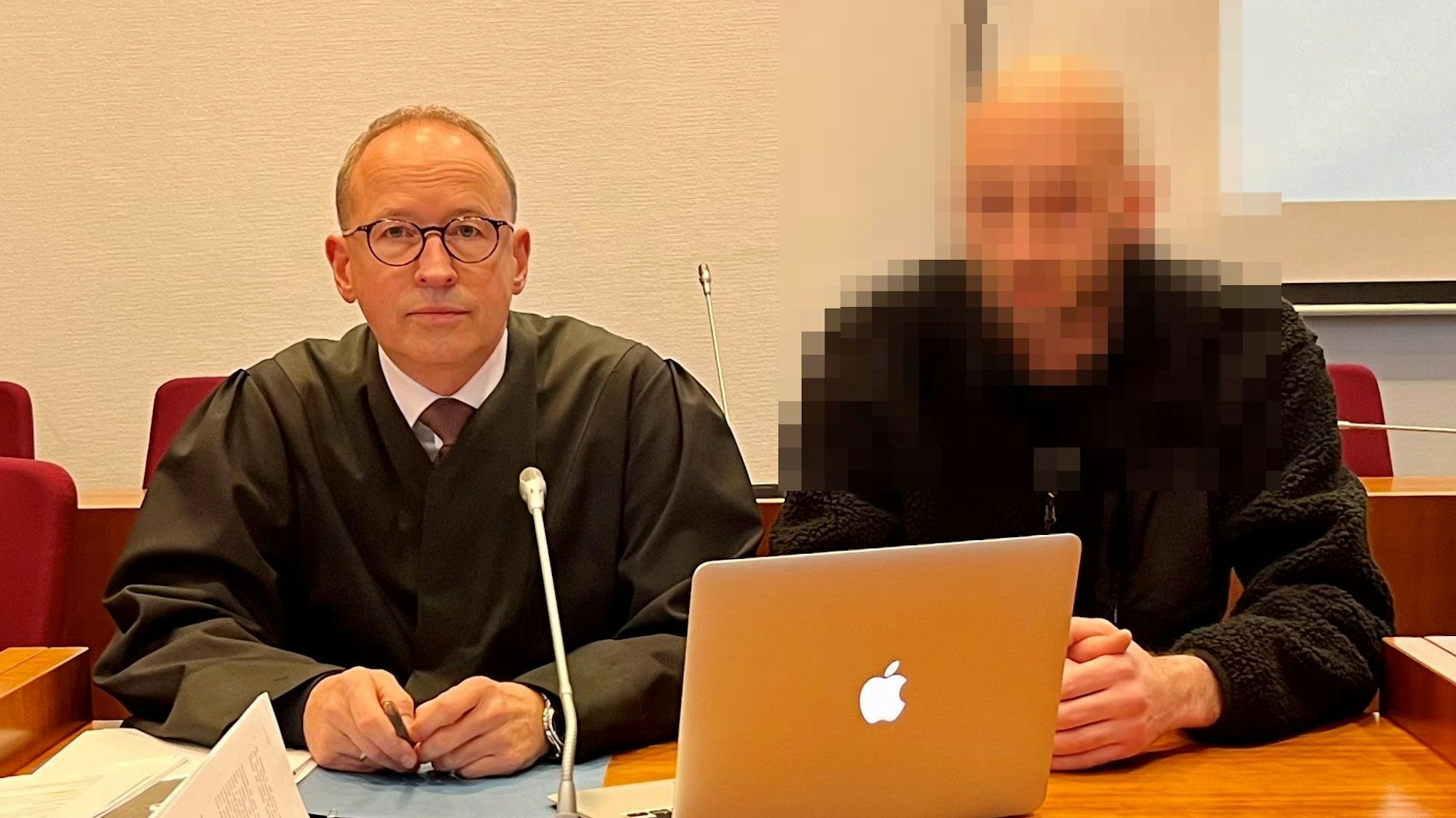 Zwei Männer sitzen an einem Tisch, auf dem ein Mikrofon und ein Laptop stehen.