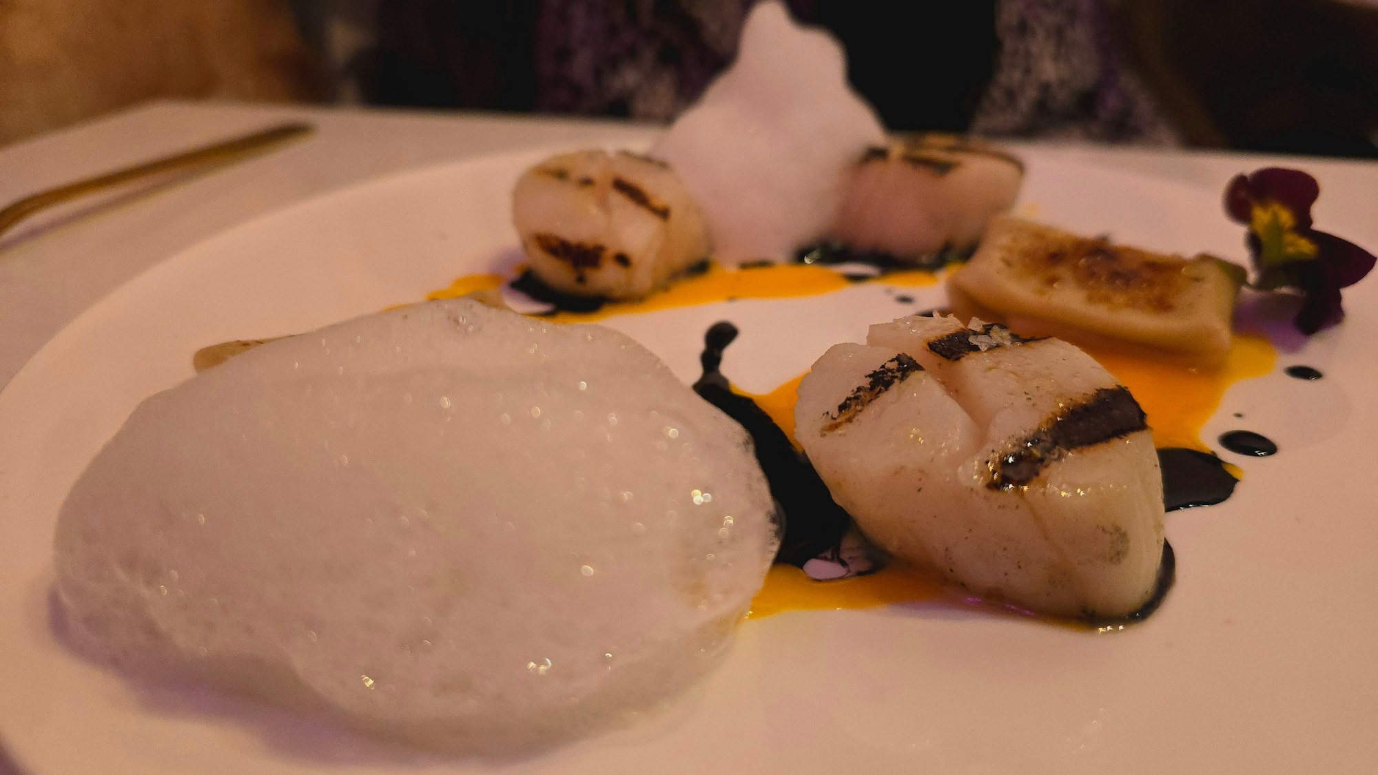 Auf einem Teller sind gebratene Jakobsmuscheln und karamellisierte WanTan-Ravioli angerichtet.