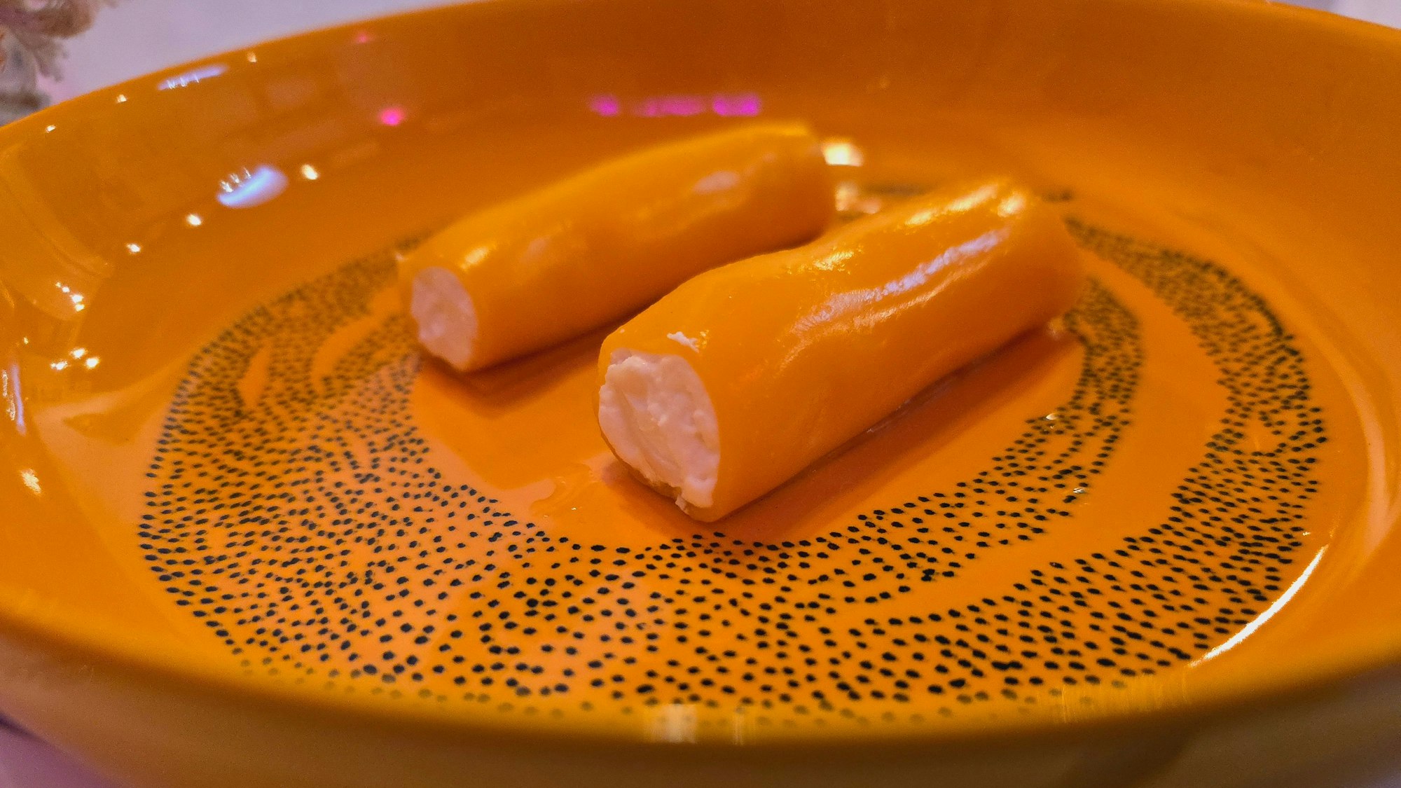 Auf einem orangenen Teller sind Mango-Cannelloni gefüllt mit Ziegenkäse angerichtet.