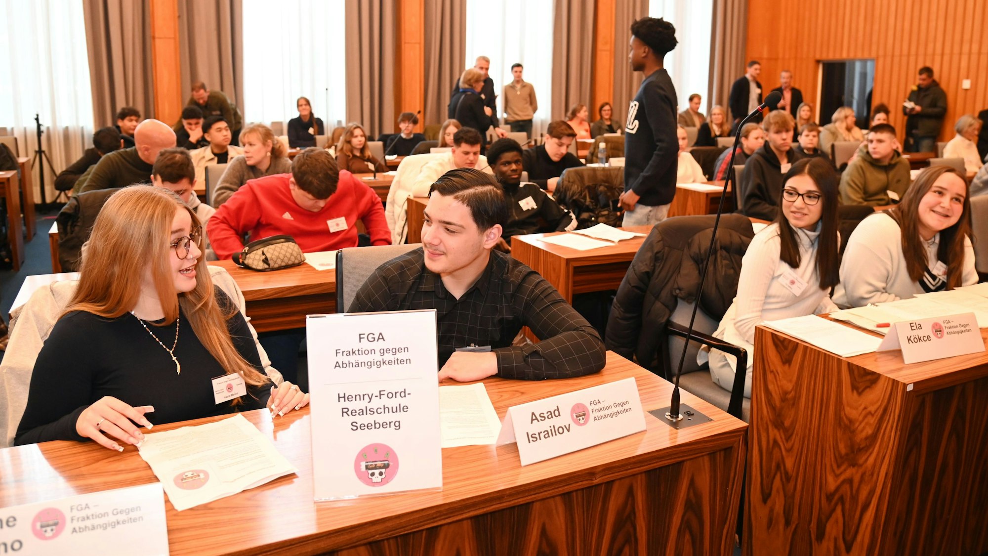 Zu sehen sind mehrere Jugendliche, die an Tischen sitzen und sich beraten.