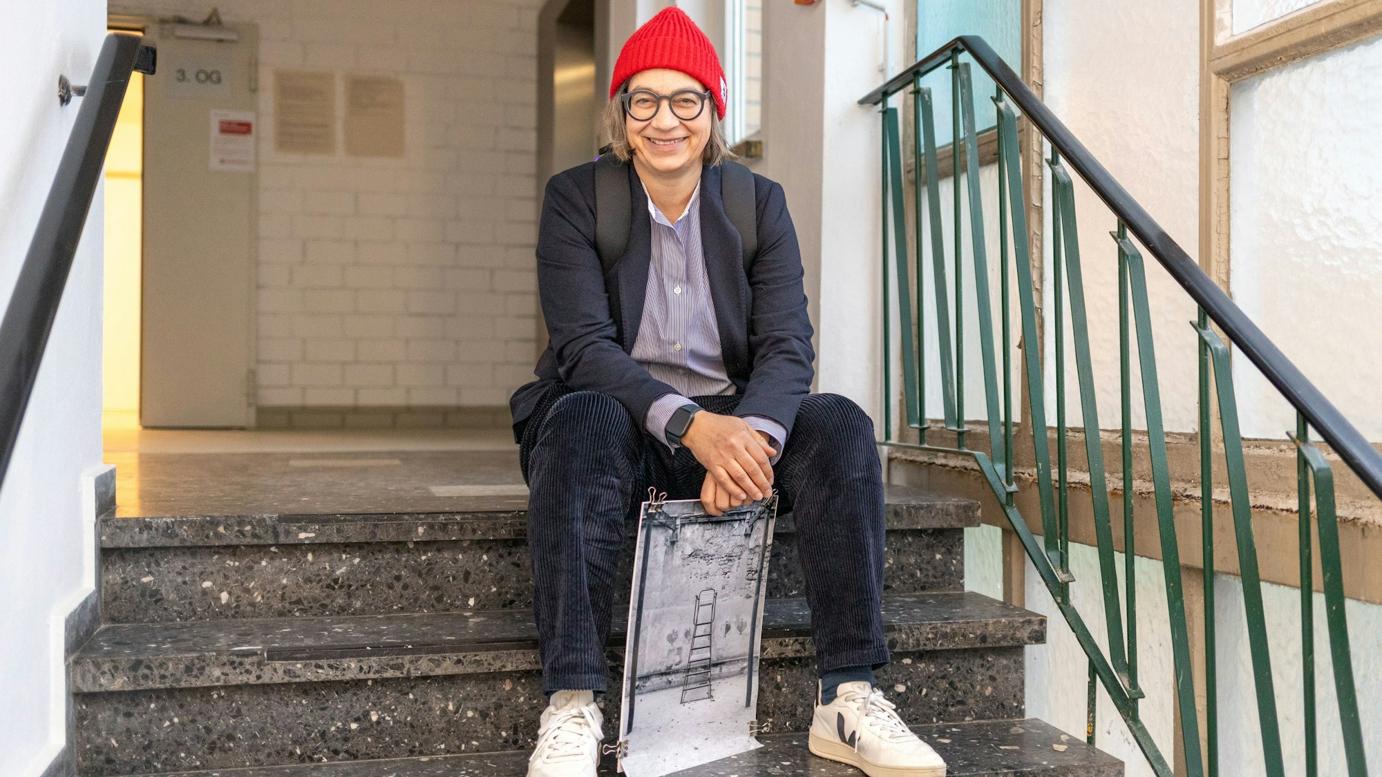 Claudia Mewaldt sitzt mit einem ihrer Bilder auf einer Treppe  im Treppenhaus.