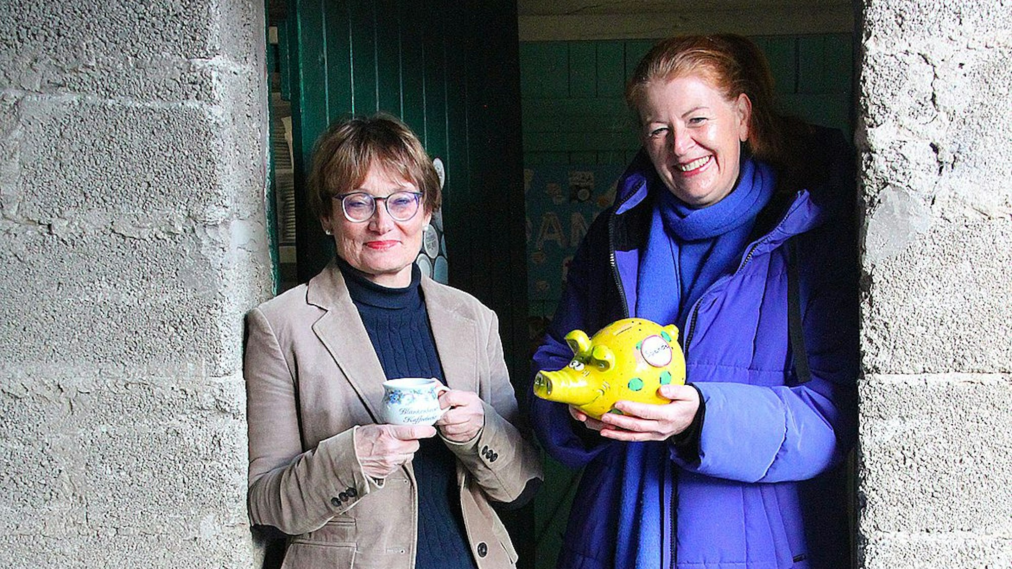 Simone Böhm mit einer Tasse in der Hand und Judith Maur mit dem Spendenschwein stehen nebeneinander.