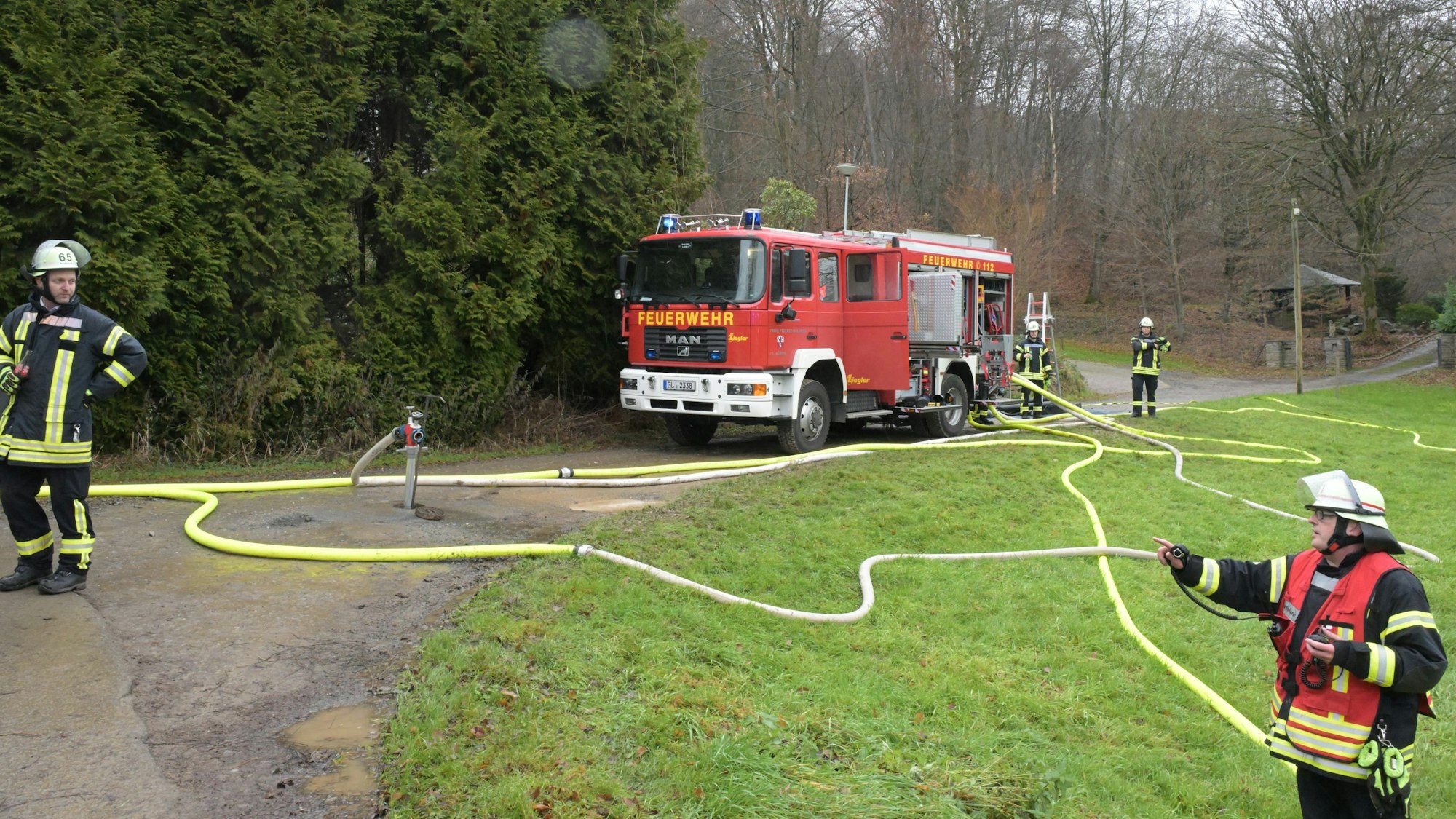 Ein Feuerwehrfahrzeug steht auf einer Nebenstraße. Schläuche verlaufen über den Boden.