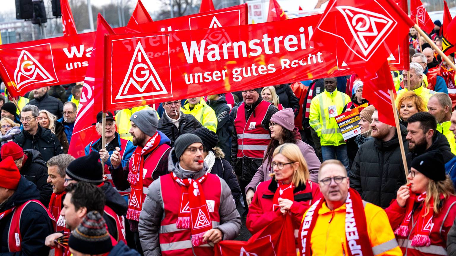 Auf dem Bild sind Streikende zu sehen, die mit roten Schals, Westen und Bannern ausgerüstet sind. (Symbolbild)