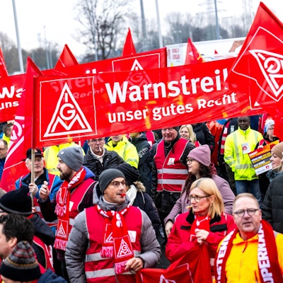 Auf dem Bild sind Streikende zu sehen, die mit roten Schals, Westen und Bannern ausgerüstet sind. (Symbolbild)