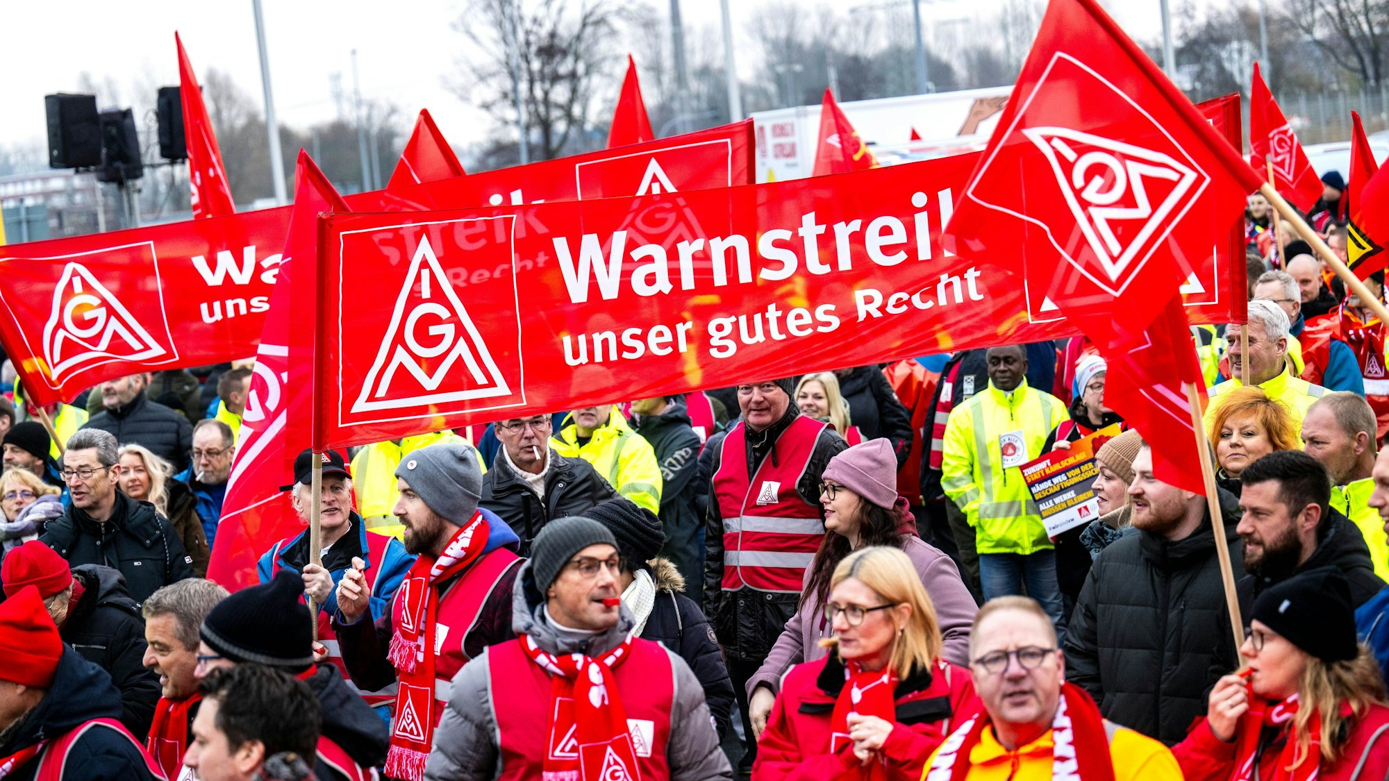 Auf dem Bild sind Streikende zu sehen, die mit roten Schals, Westen und Bannern ausgerüstet sind. (Symbolbild)