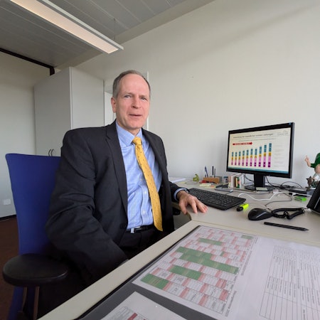 Ingo Hessenius sitzt an seinem Schreibtisch in der Kreisverwaltung. Im Hintergrund auf einem Bildschirm ist ein Säulendiagramm zu sehen, das den Anstieg der Sozialausgaben für den Kreis verdeutlicht.