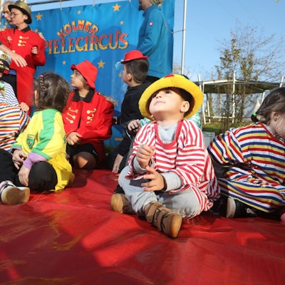 Mehrere Kinder sitzen mit geringelten T-Shirts und bunten Hüten in der Manege des Kölner Spielecircus e.V.