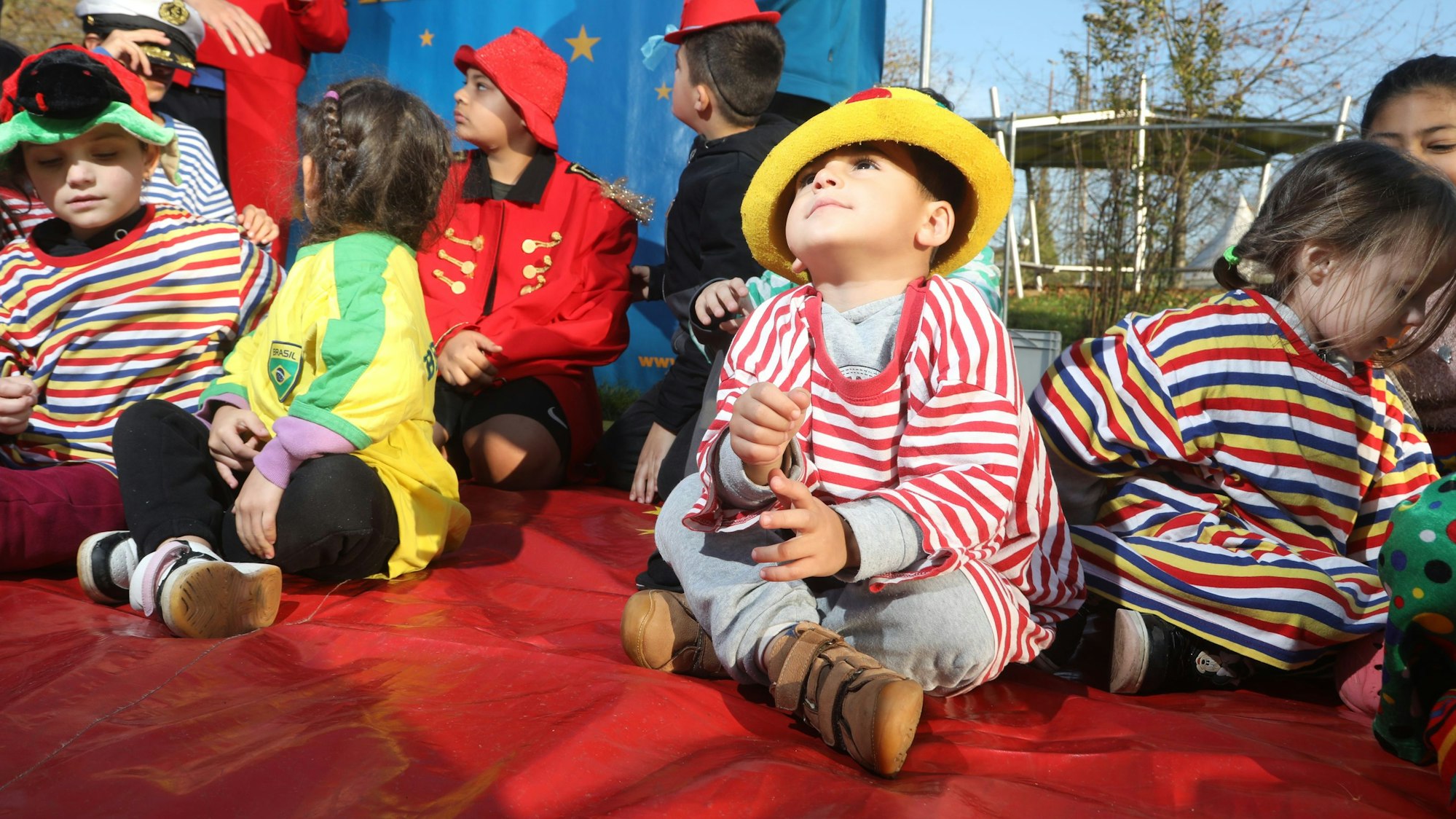 Mehrere Kinder sitzen mit geringelten T-Shirts und bunten Hüten in der Manege des Kölner Spielecircus e.V.