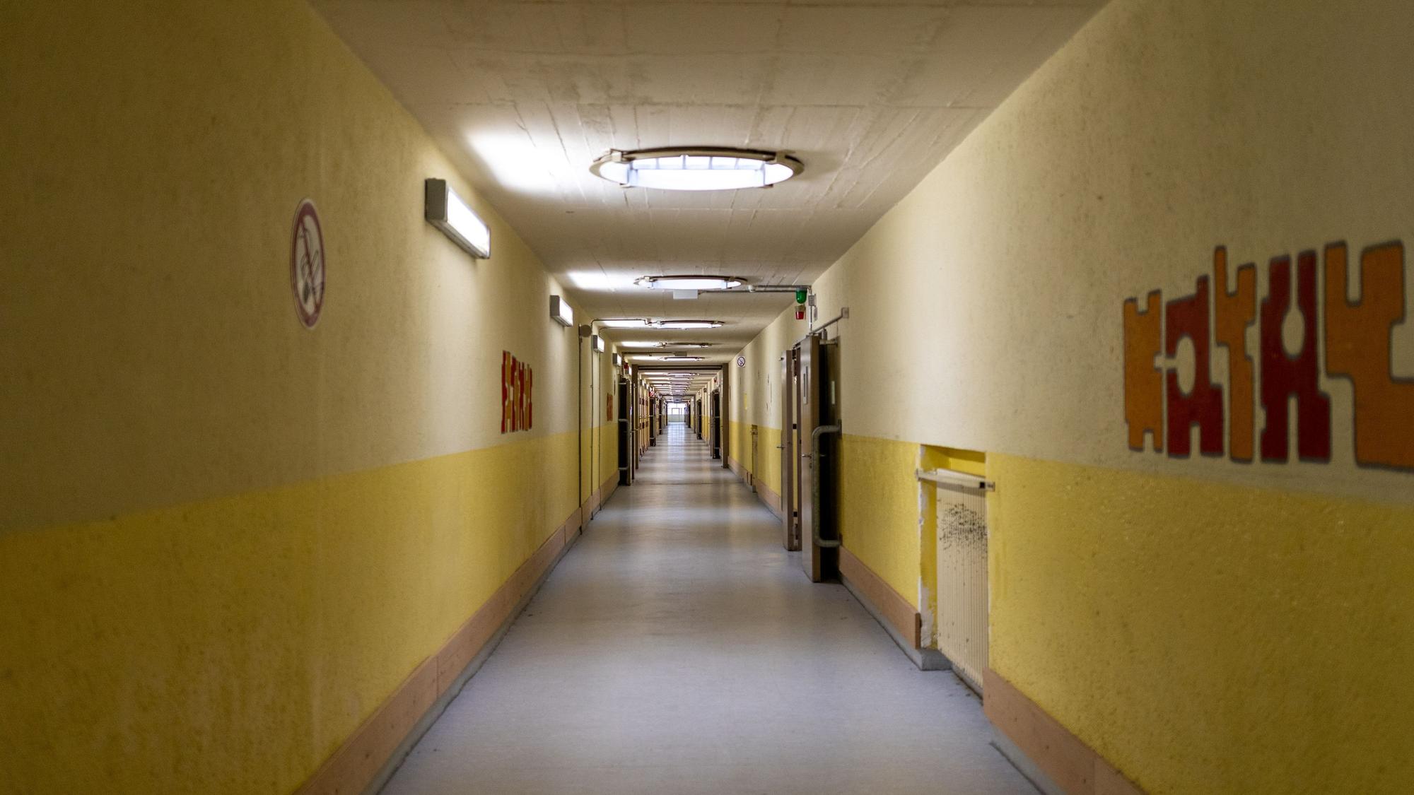 Ein langer Gang mit Zellen. Die Wände sind gelb und beige.