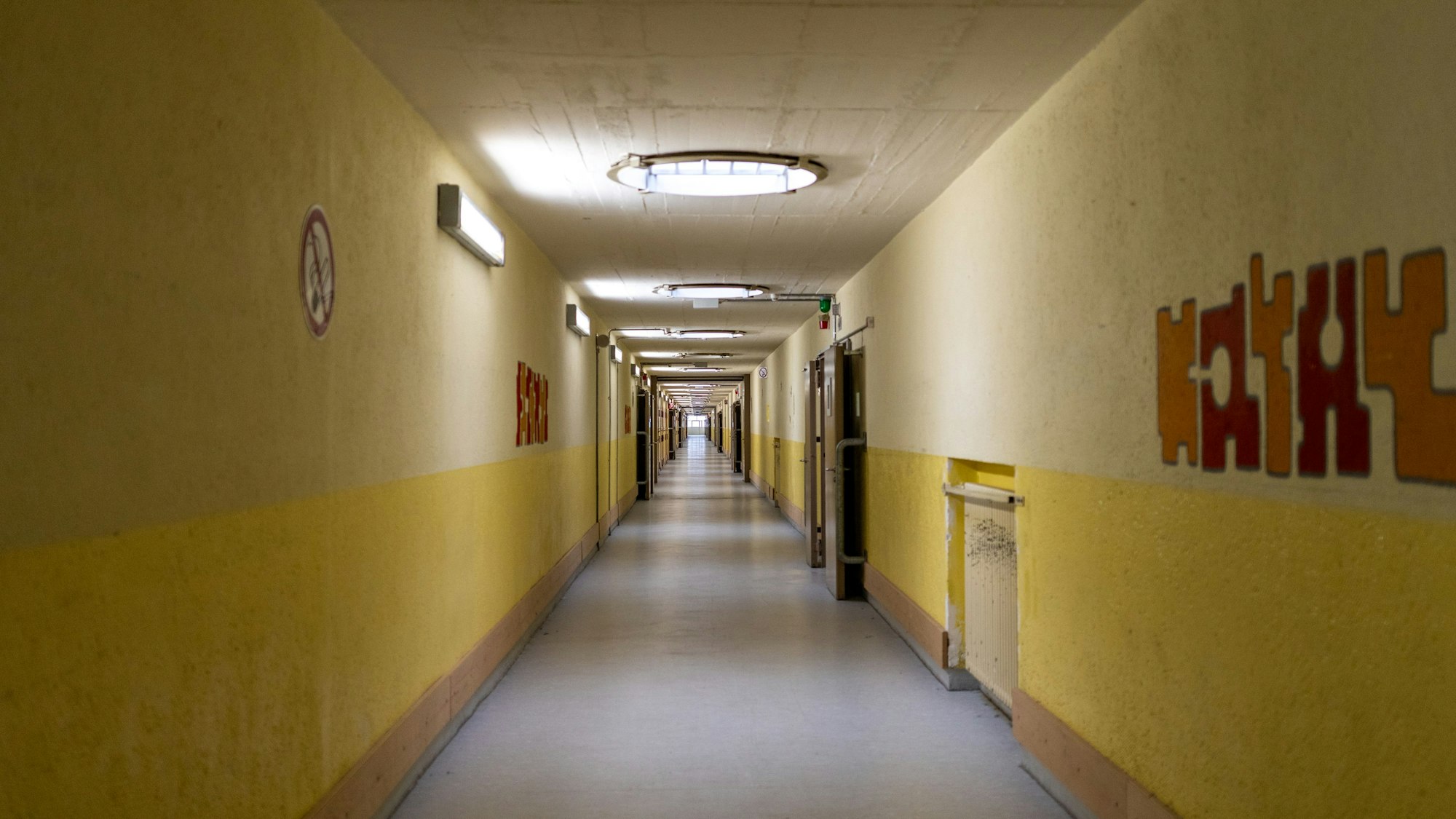 Ein langer Gang mit Zellen. Die Wände sind gelb und beige.
