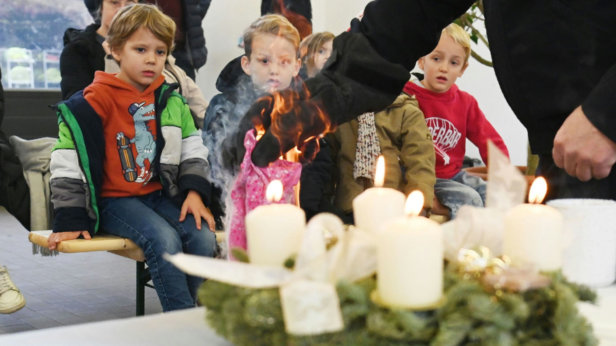 Mehrere Kinder bekommen vorgeführt, wie schnell ein Kleidungsstück am Adventskrank Feuer fängt.