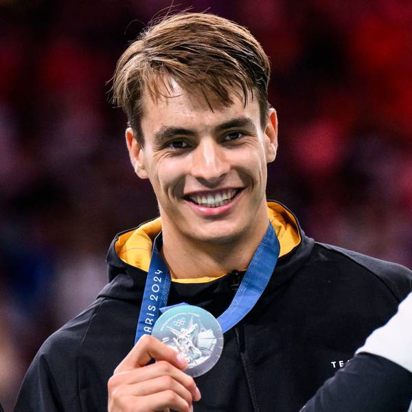 Handballer Julian Köster zeigt lächelnd seine olympische Silbermedaille in die Kamera.