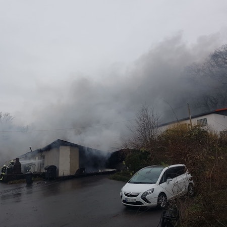Feuerwehrleute lösche eine Lagerhalle aus der Rauch herausdringt.