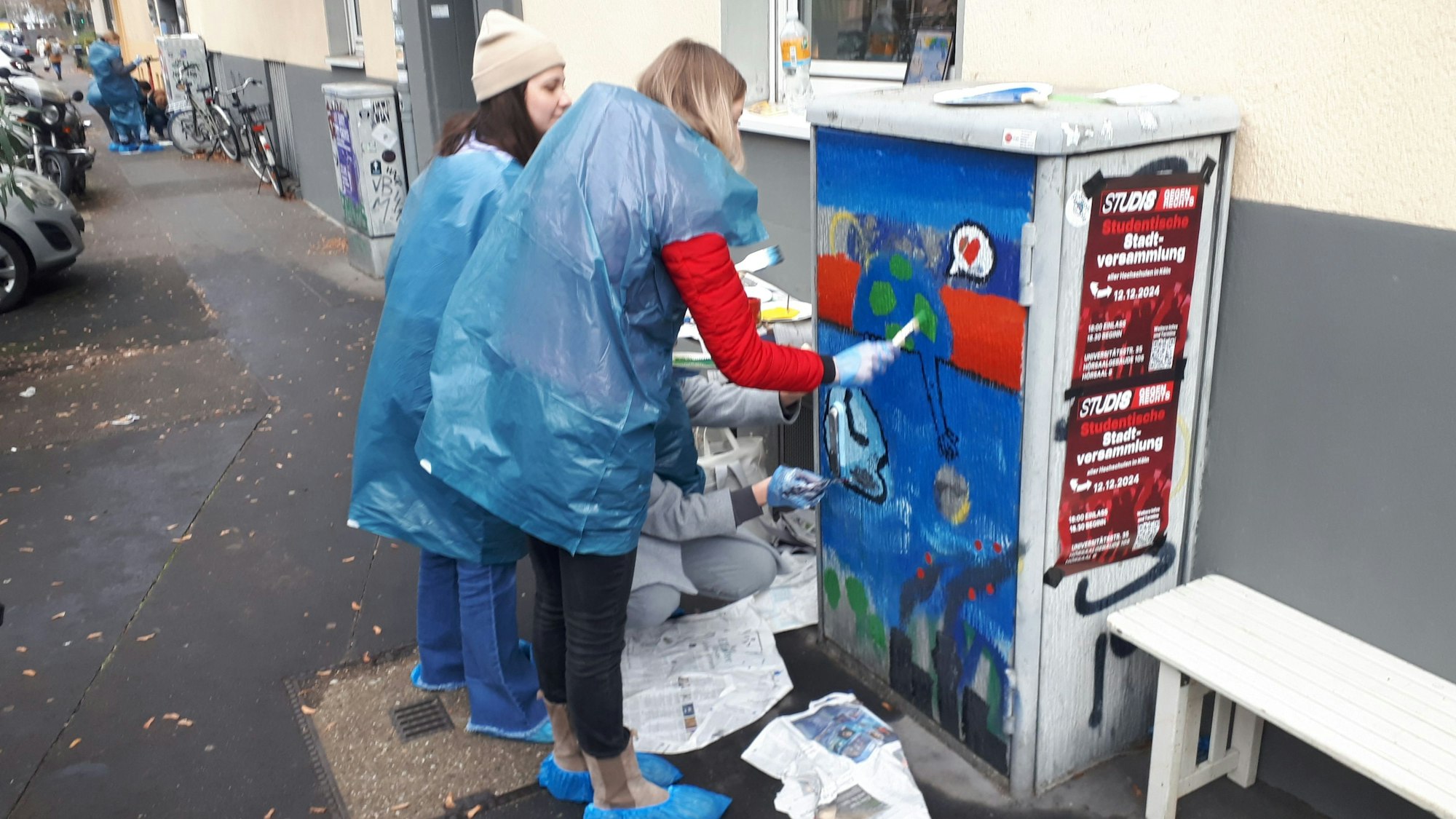 Zwei Mädchen bemalen in Schutzüberzügen einen Trafo-Kasten.