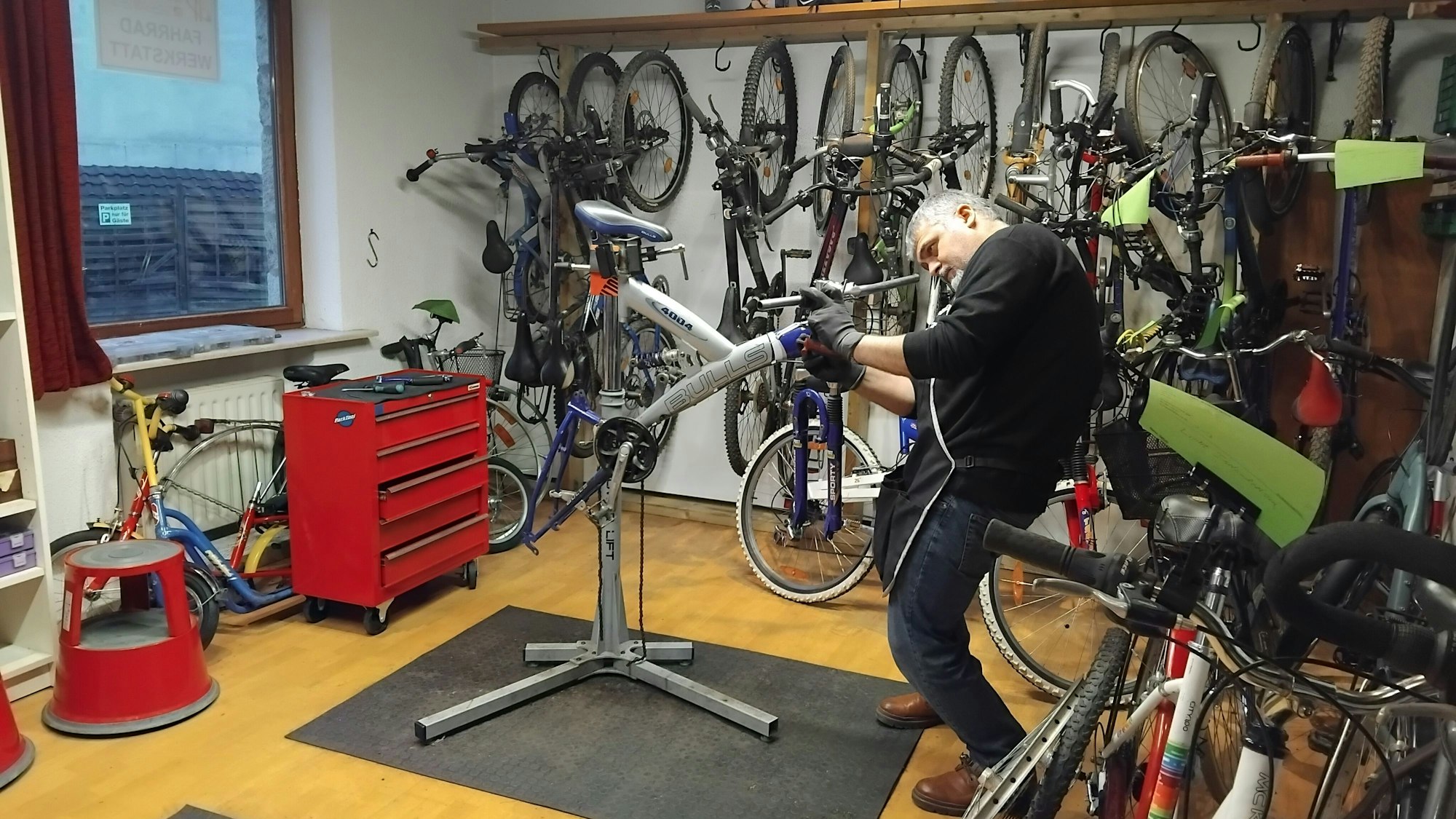 Ein Mann steht in einem Raum und schraubt an einem Fahrrad, hinter ihm sind mehrere Räder aufgehängt.