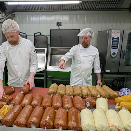 Zwei Männer ordnen Kunststoffschläuche mit Saucen auf einem Tisch.