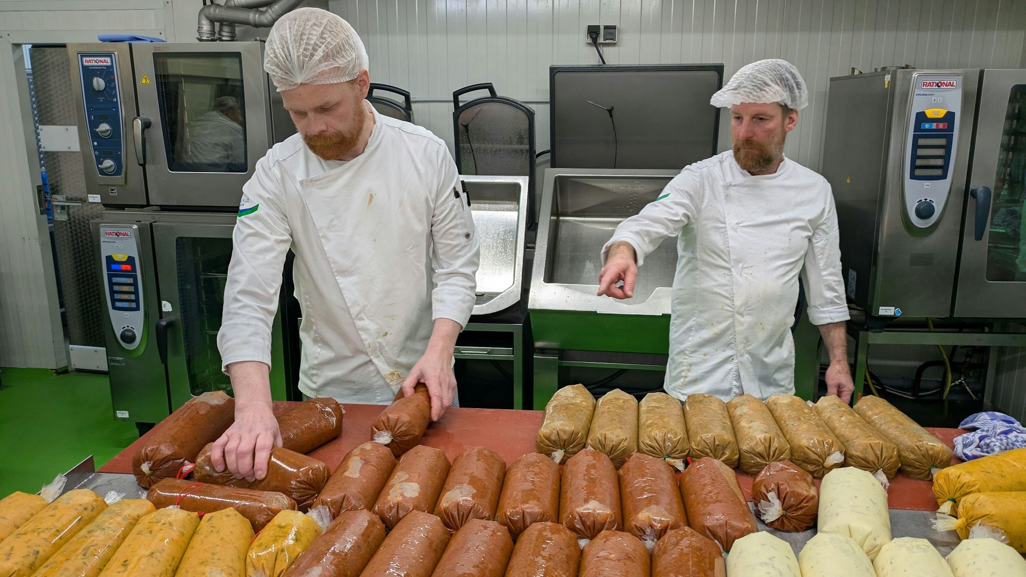 Zwei Männer ordnen Kunststoffschläuche mit Saucen auf einem Tisch.