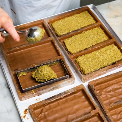 PRODUKTION - 27.11.2024, Niedersachsen, Hannover: Eine Mitarbeiterin der Manufatur Trüffel Güse befüllt bei der Herstellung von Dubai-Schokolade die Schokoladentafeln mit einer Creme aus Pistazienmus und Engelshaar. Bei den Schokoladenherstellern laufen die Weihnachtsvorbereitungen auf Hochtouren. Der Hype rund um die Dubai-Schokoladen ist dabei ungebrochen. (zu dpa: «Weihnachten wird orientalisch: Dubai-Schokolade statt Schnee») Foto: Alicia Windzio/dpa +++ dpa-Bildfunk +++