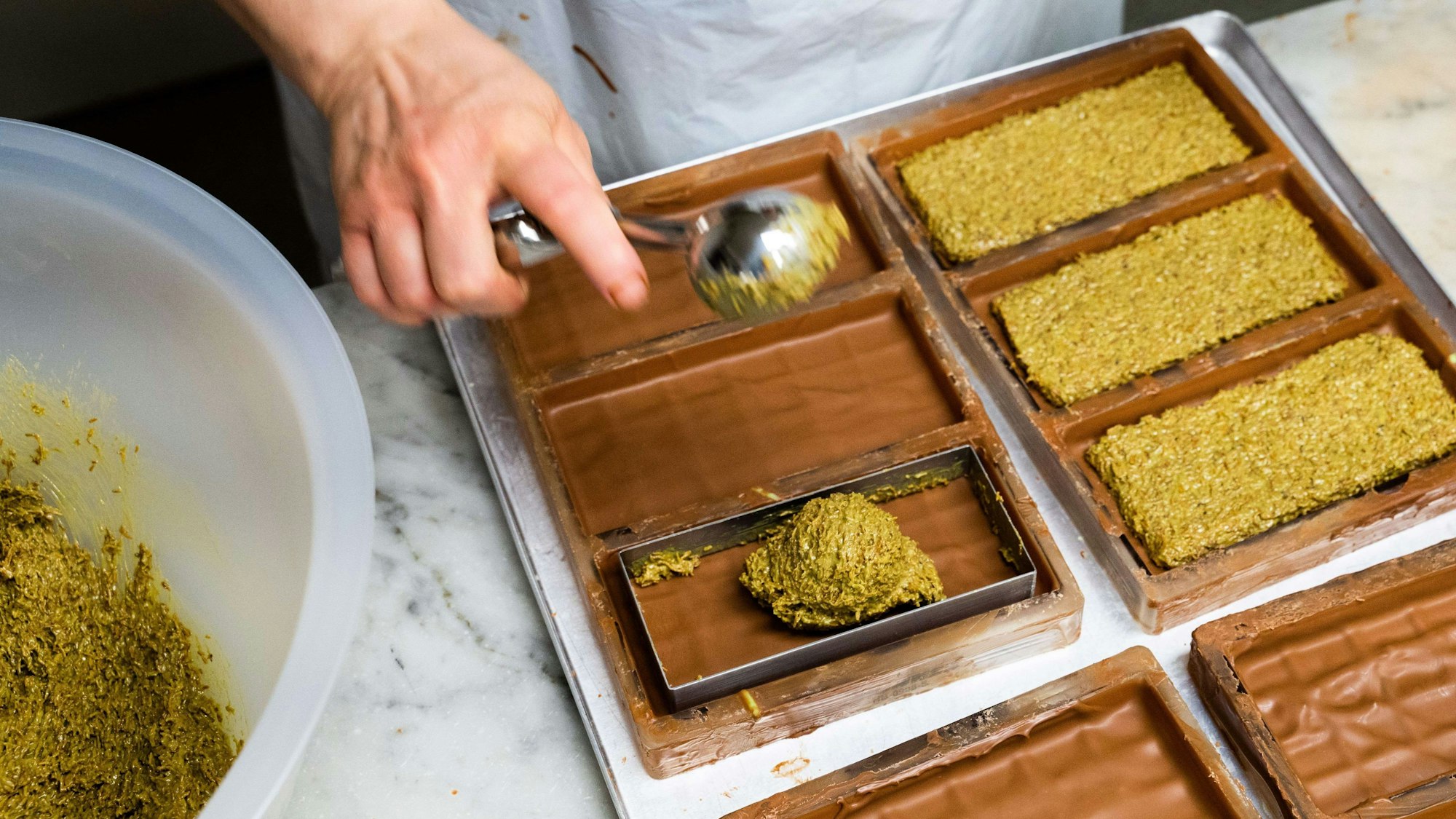 Eine Mitarbeiterin der Manufatur Trüffel Güse befüllt bei der Herstellung von Dubai-Schokolade die Schokoladentafeln mit einer Creme aus Pistazienmus und Engelshaar.