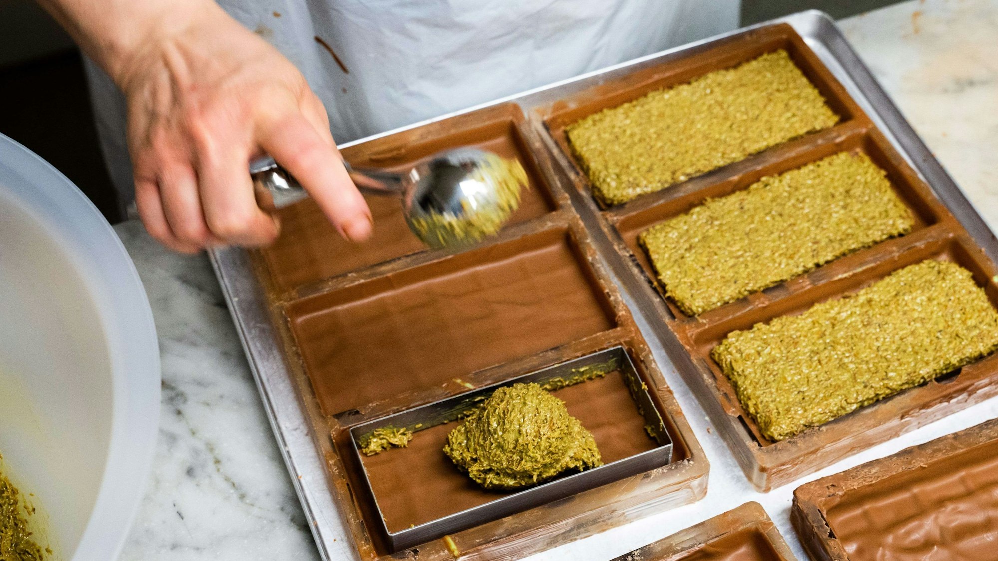 PRODUKTION - 27.11.2024, Niedersachsen, Hannover: Eine Mitarbeiterin der Manufatur Trüffel Güse befüllt bei der Herstellung von Dubai-Schokolade die Schokoladentafeln mit einer Creme aus Pistazienmus und Engelshaar. Bei den Schokoladenherstellern laufen die Weihnachtsvorbereitungen auf Hochtouren. Der Hype rund um die Dubai-Schokoladen ist dabei ungebrochen. (zu dpa: «Weihnachten wird orientalisch: Dubai-Schokolade statt Schnee») Foto: Alicia Windzio/dpa +++ dpa-Bildfunk +++