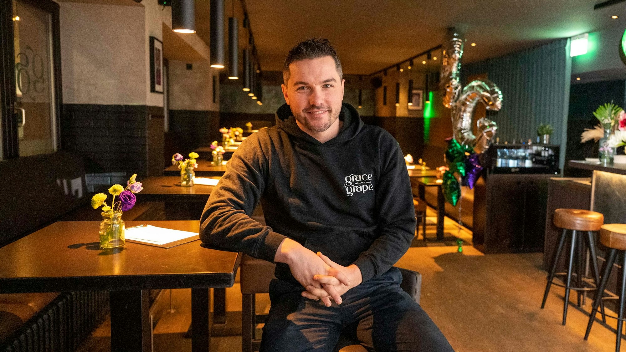 Chef Stephan Hinz sitzt auf einem Barhocker an einem Tisch im Grace & Grape.