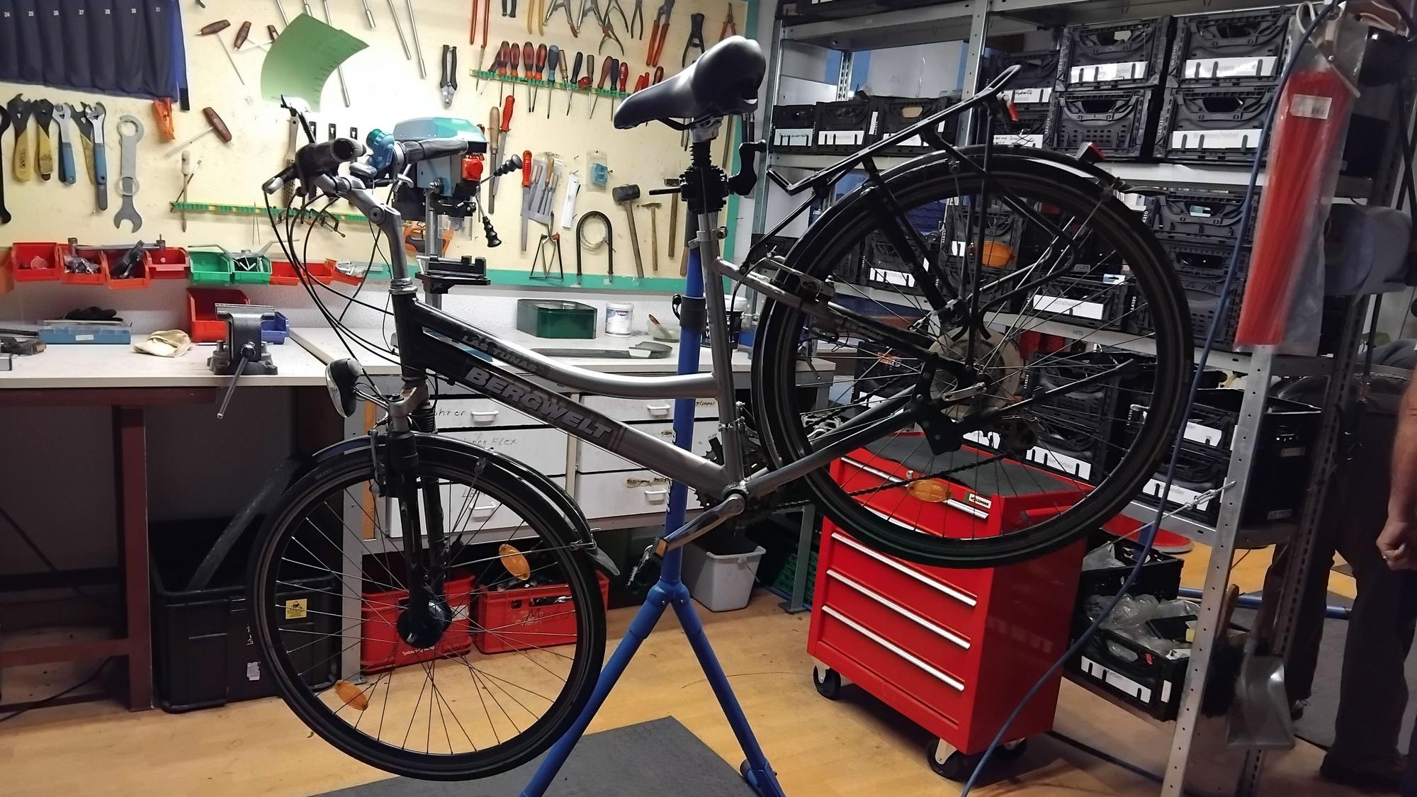 Ein Fahrrad ist zur Reparatur auf einen Ständer gespannt, im Hintergrund sieht man Werkzeug