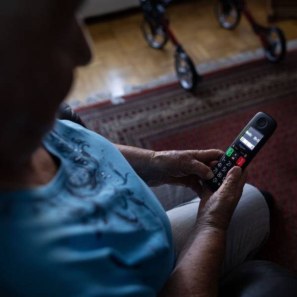 Eine alte Frau guckt auf ein Festnetz-Telefon.