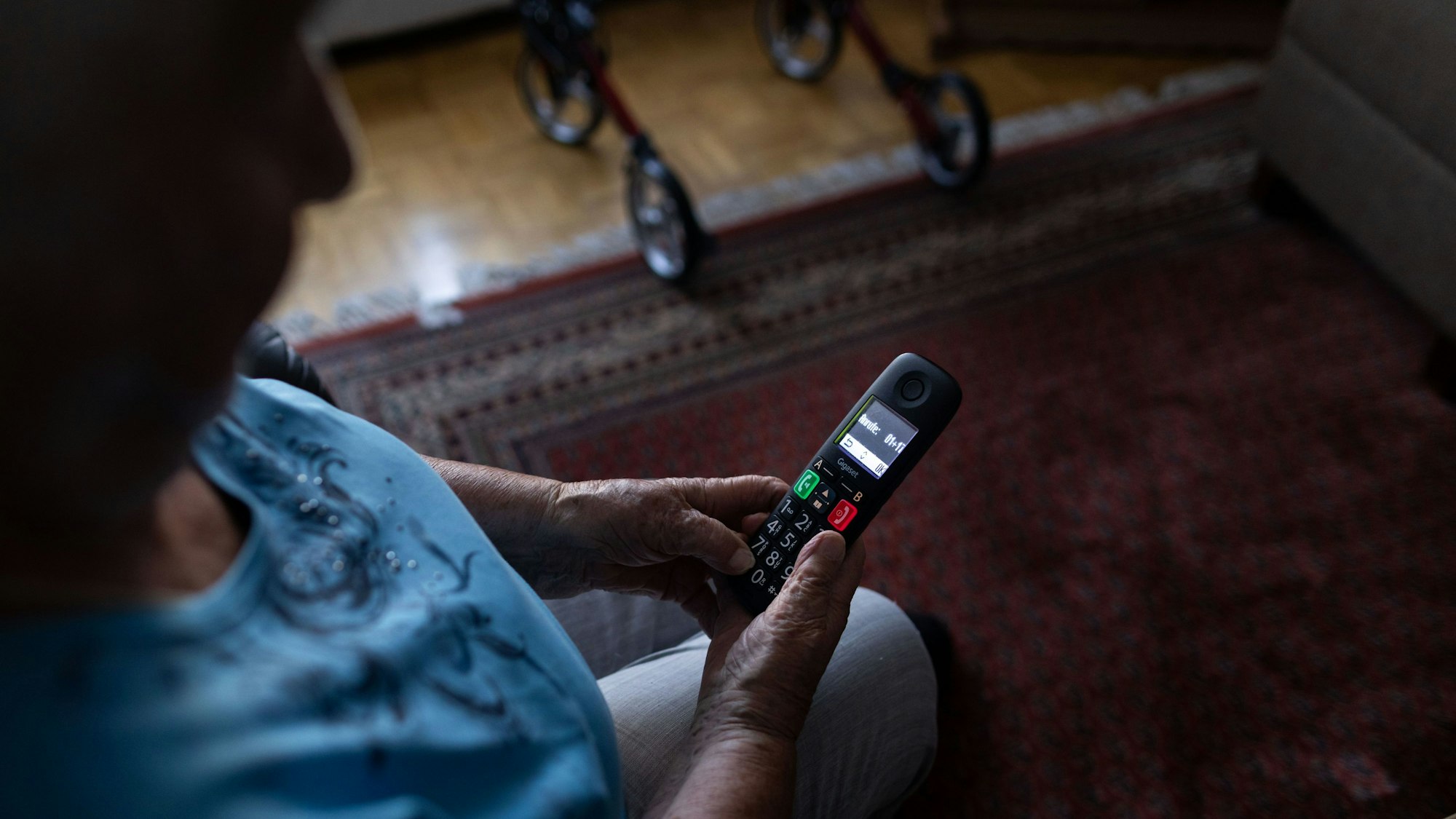 Eine alte Frau guckt auf ein Festnetz-Telefon.