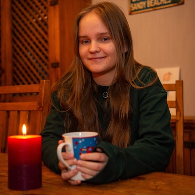 Kira Grohs sitzt mit einer Weihnachtstasse in den Händen am Esstisch ihrer Eltern, vor ihr brennt eine Kerze.